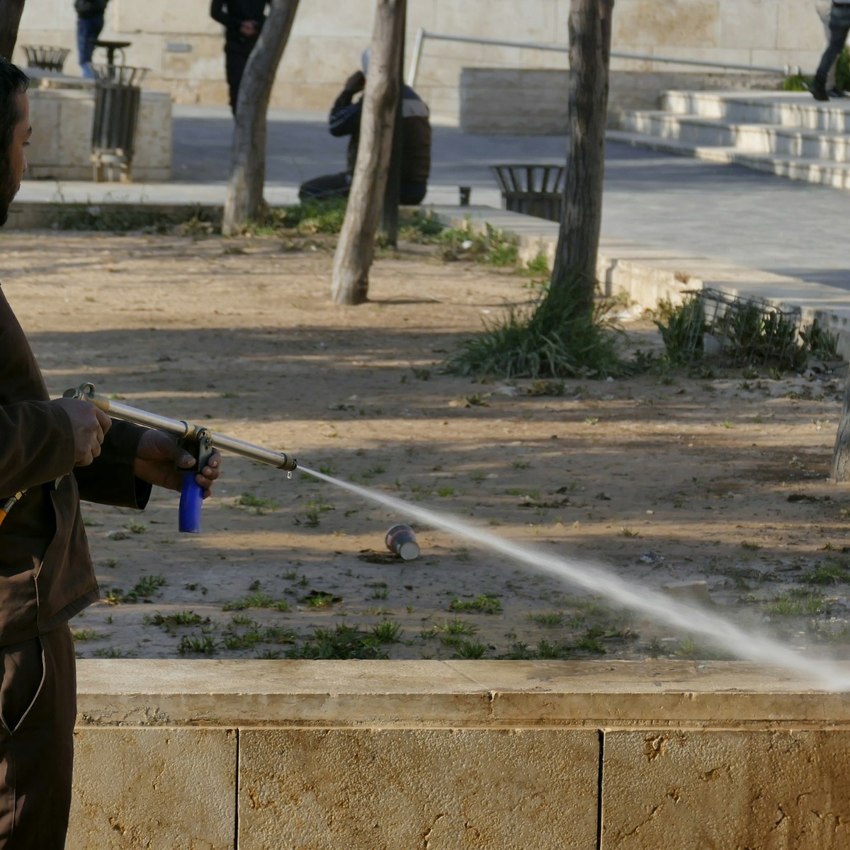 Worker using a high-pressure water spray wand to clean an outdoor concrete surface during pressure washing services in Cunningham, TN