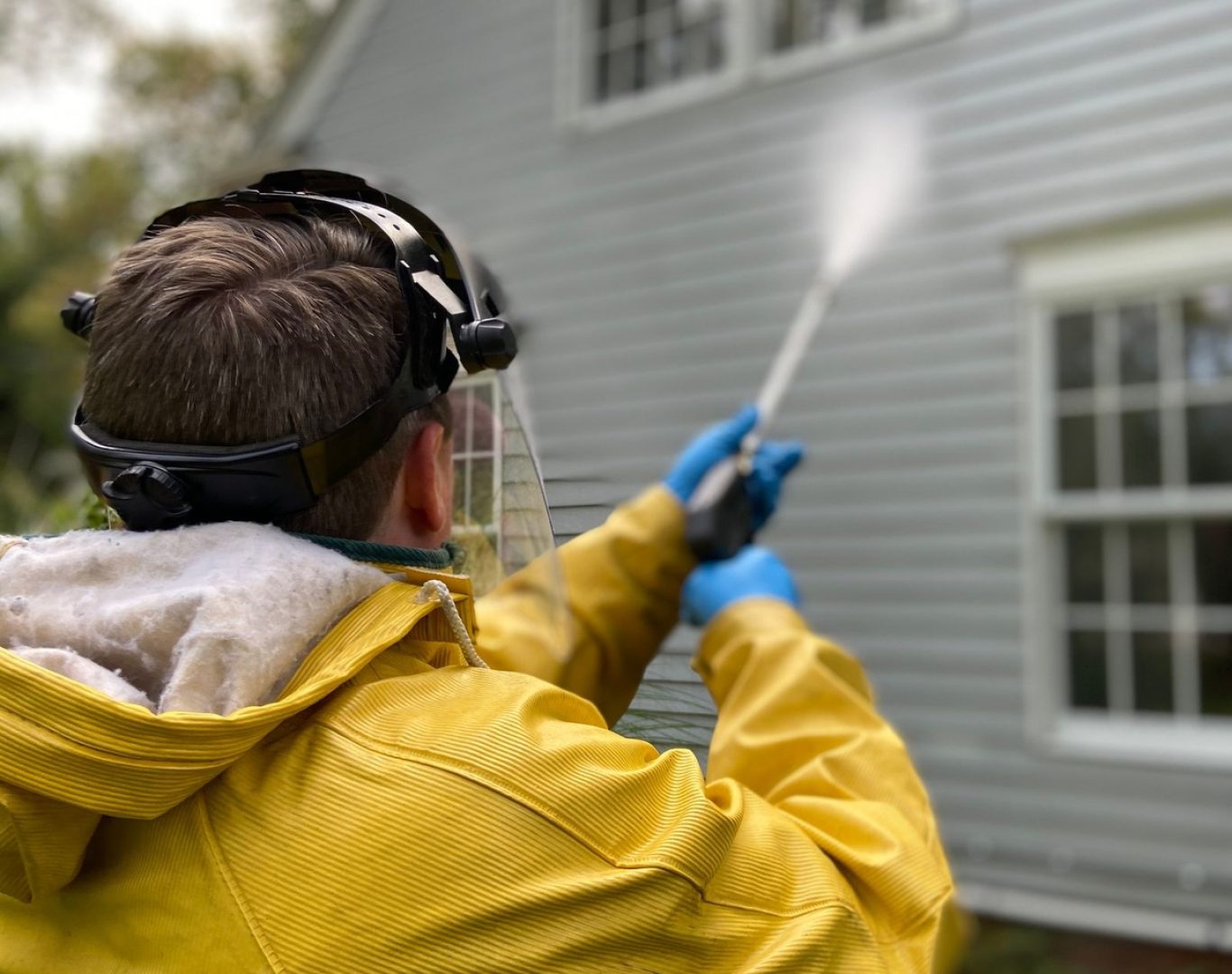 Worker wearing protective gear pressure washing the exterior siding of a house during pressure washing services near me