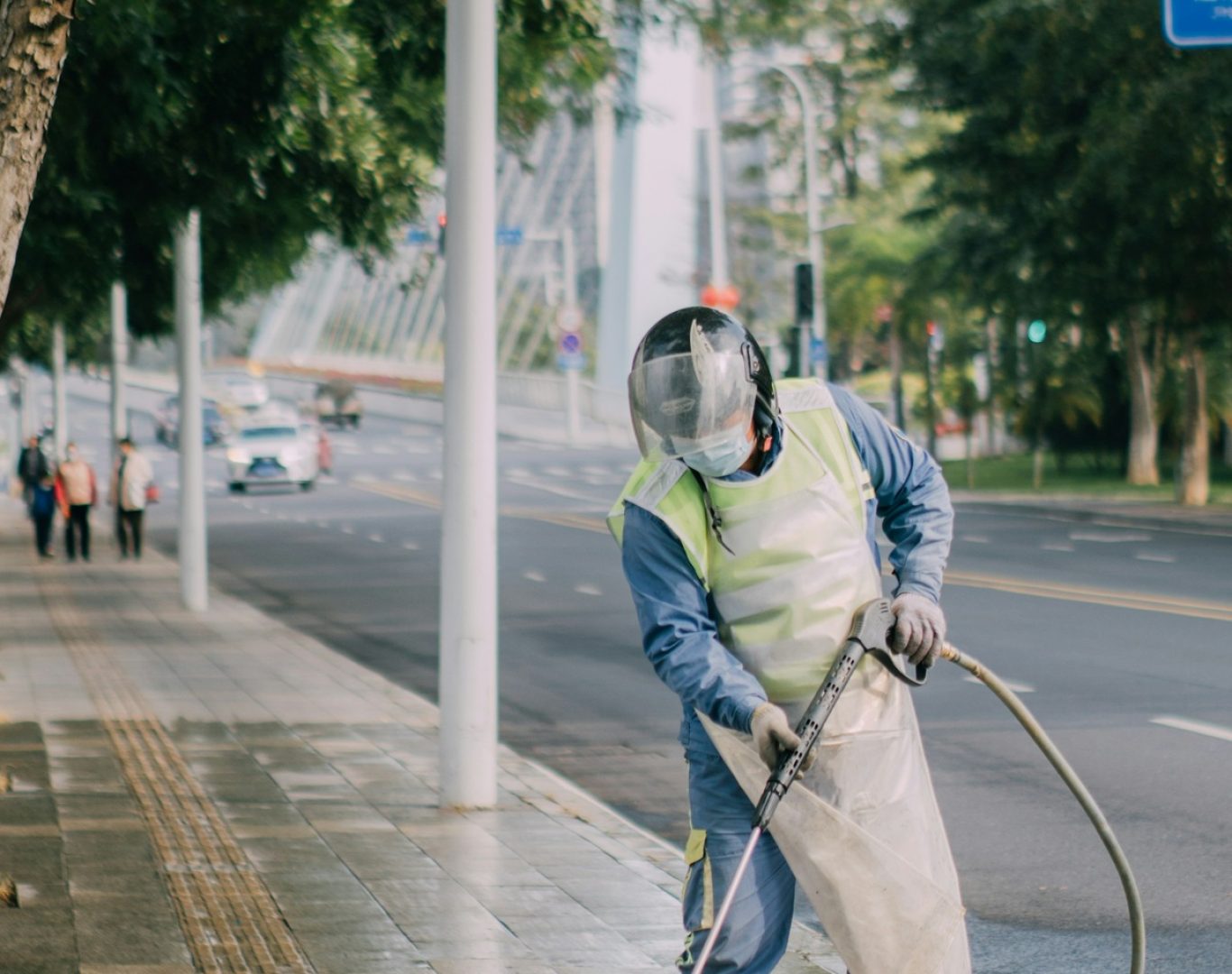 Worker wearing protective gear pressure washing a concrete sidewalk with a high-pressure spray wand during pressure washing services near me